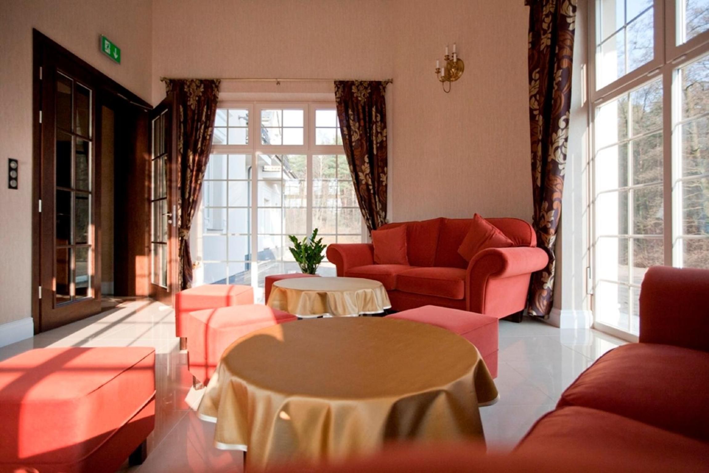 Una habitación de hotel con un sofá rojo, una mesita redonda y un ventanal con cortinas.