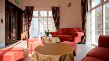 Una habitación de hotel con un sofá rojo, una mesita redonda y un ventanal con cortinas.