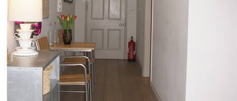 Een smalle gang met een eettafel en stoelen, een klein kastje, een vaas met bloemen en een brandblusser.