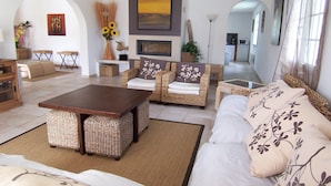 A living room with a sofa, two armchairs, a coffee table, and a fireplace. There are decorative items like sunflowers and a vase on the mantel.