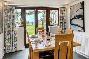 A dining area with a table set for four, a vase with flowers, and a view of the outdoors. - Courtyard Barn 5* rated in stunning rural location on Somerset, Dorset  border. (Horsington)