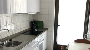 Ett kompakt kök med vita skåp, en bänkskiva i granit, en diskho, en spis och en matplats med ett bord och stolar.