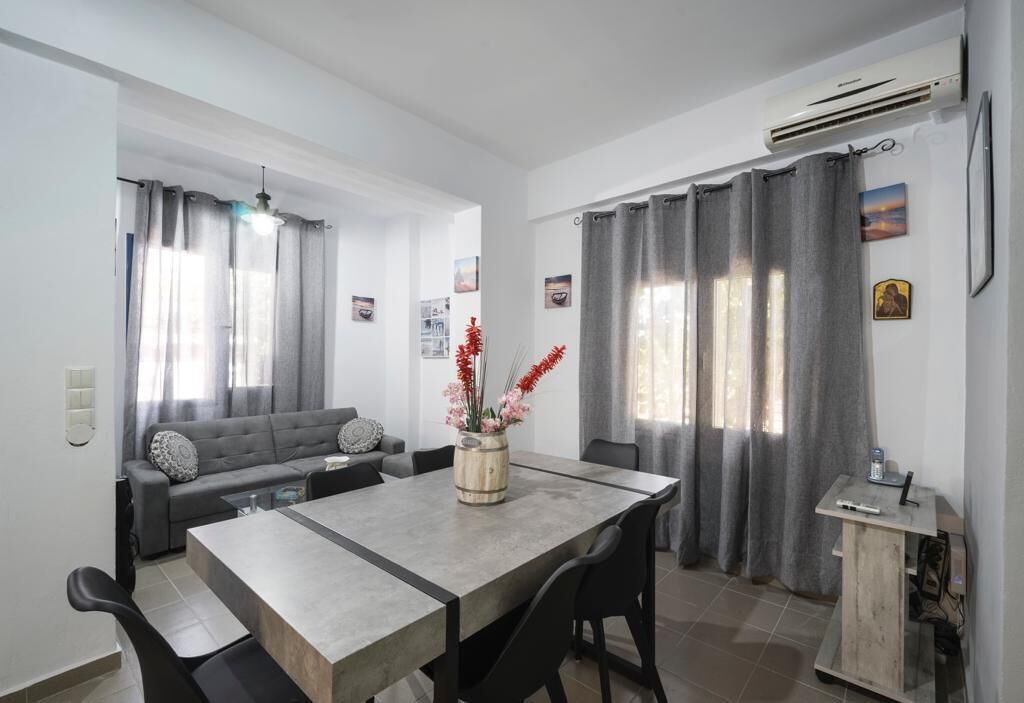 A modern living room with a grey sofa, a dining table with chairs, and a small wooden cabinet.