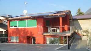 Ein rotes Gebäude mit einem grünen Rollo, einer Sat-Anlage und einer Treppe, die zu einem Balkon führt.