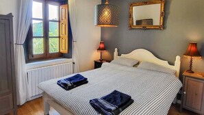 A bedroom with a bed, two bedside tables, a hanging lamp, a window with curtains, and a mirror on the wall.