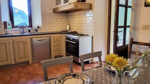 A kitchen with a dishwasher, stove, and sink. There is a dining table with plates and a vase of flowers.