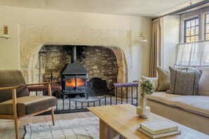 A cozy living room with a stone fireplace, leather armchair, sofa, and a table with books.