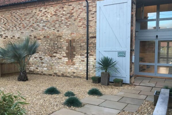 A stone building with a wooden door and a metal gate. - Owlets at Mulberry Barn, Heacham, Norfolk (King's Lynn)