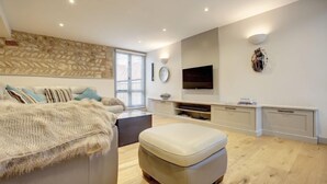 Un soggiorno moderno con una parete in pietra a contrasto, un'ampia televisione a schermo piatto, un divano con una coperta e un pavimento in legno.