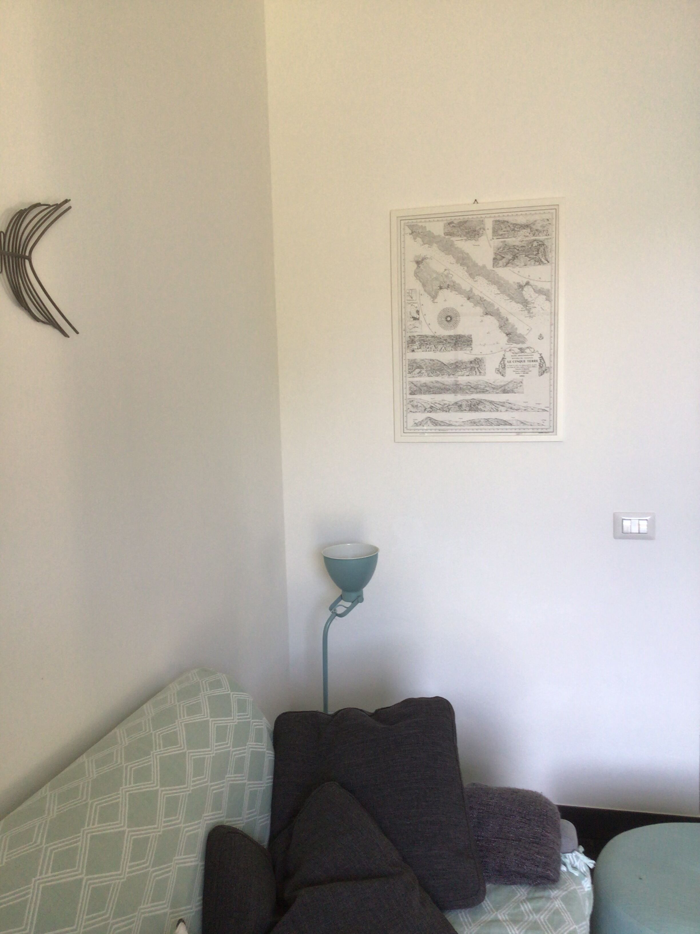 A room with a patterned sofa, a wall-mounted lamp, and a framed map.