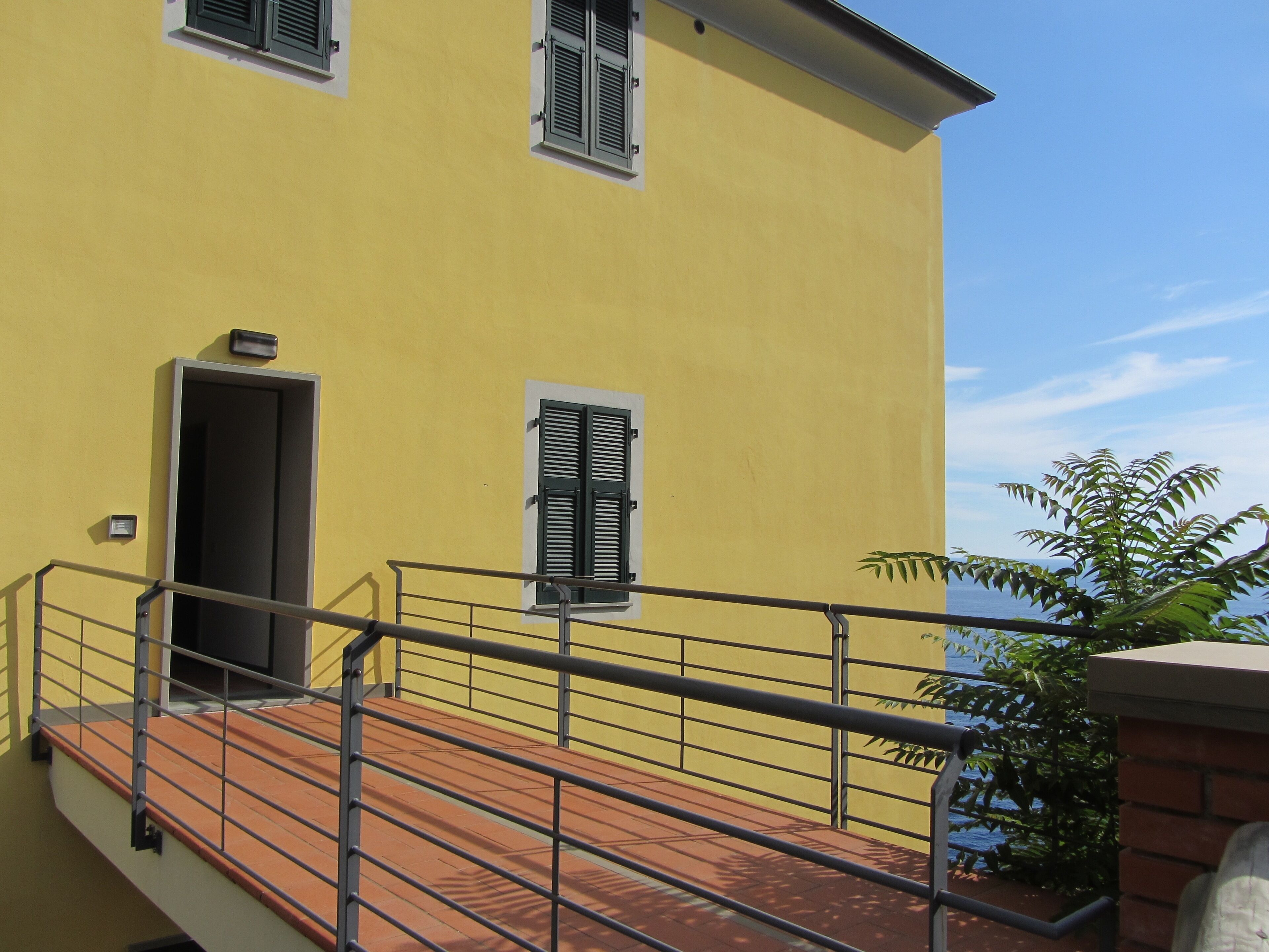 Um edifício amarelo com varanda, porta e janela com persianas.