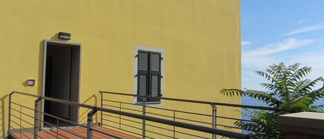Um edifício amarelo com varanda, porta e janela com persianas.