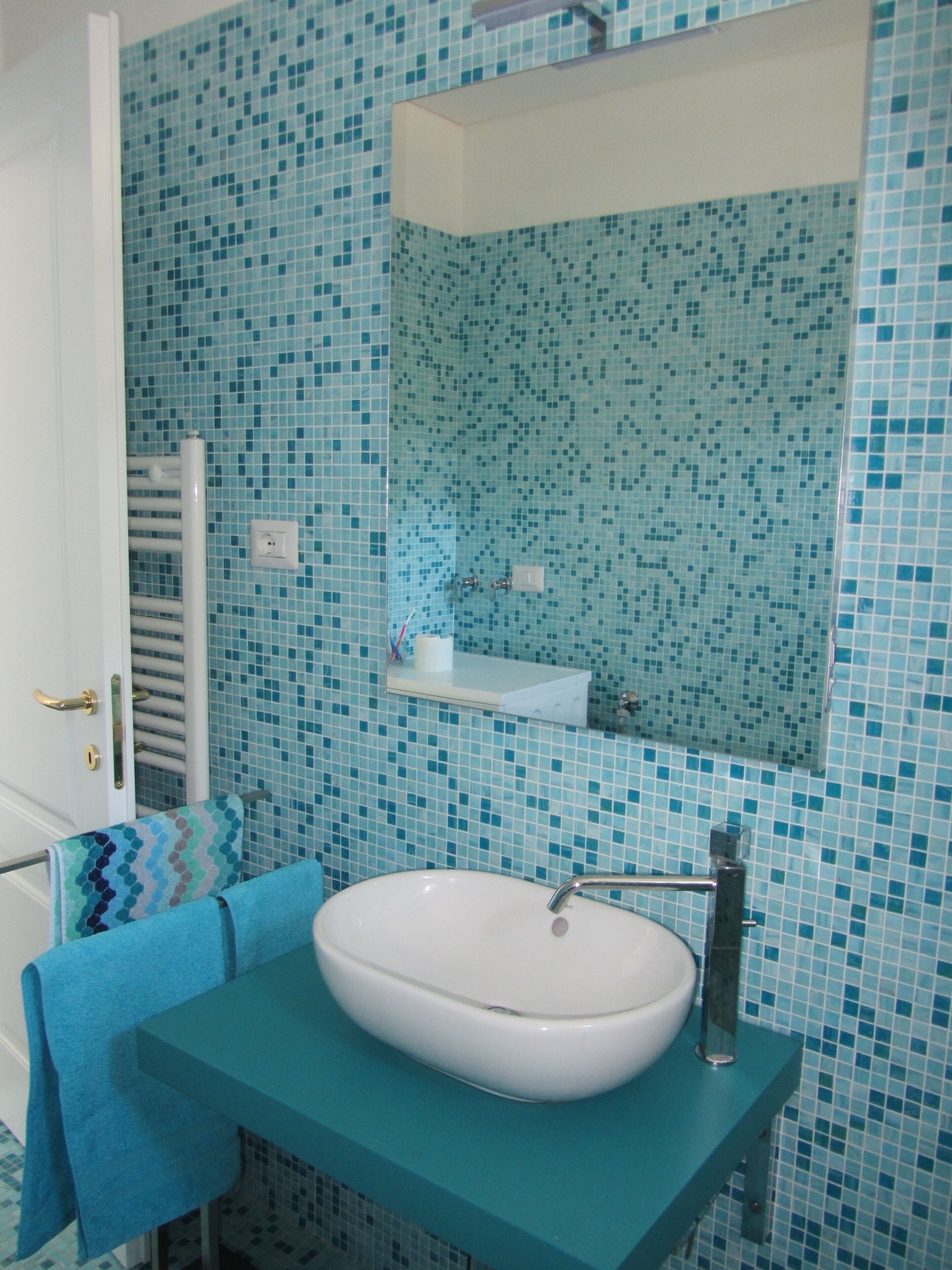 Un baño con lavamanos blanco, paredes con azulejos azules, un perchero y un espejo.
