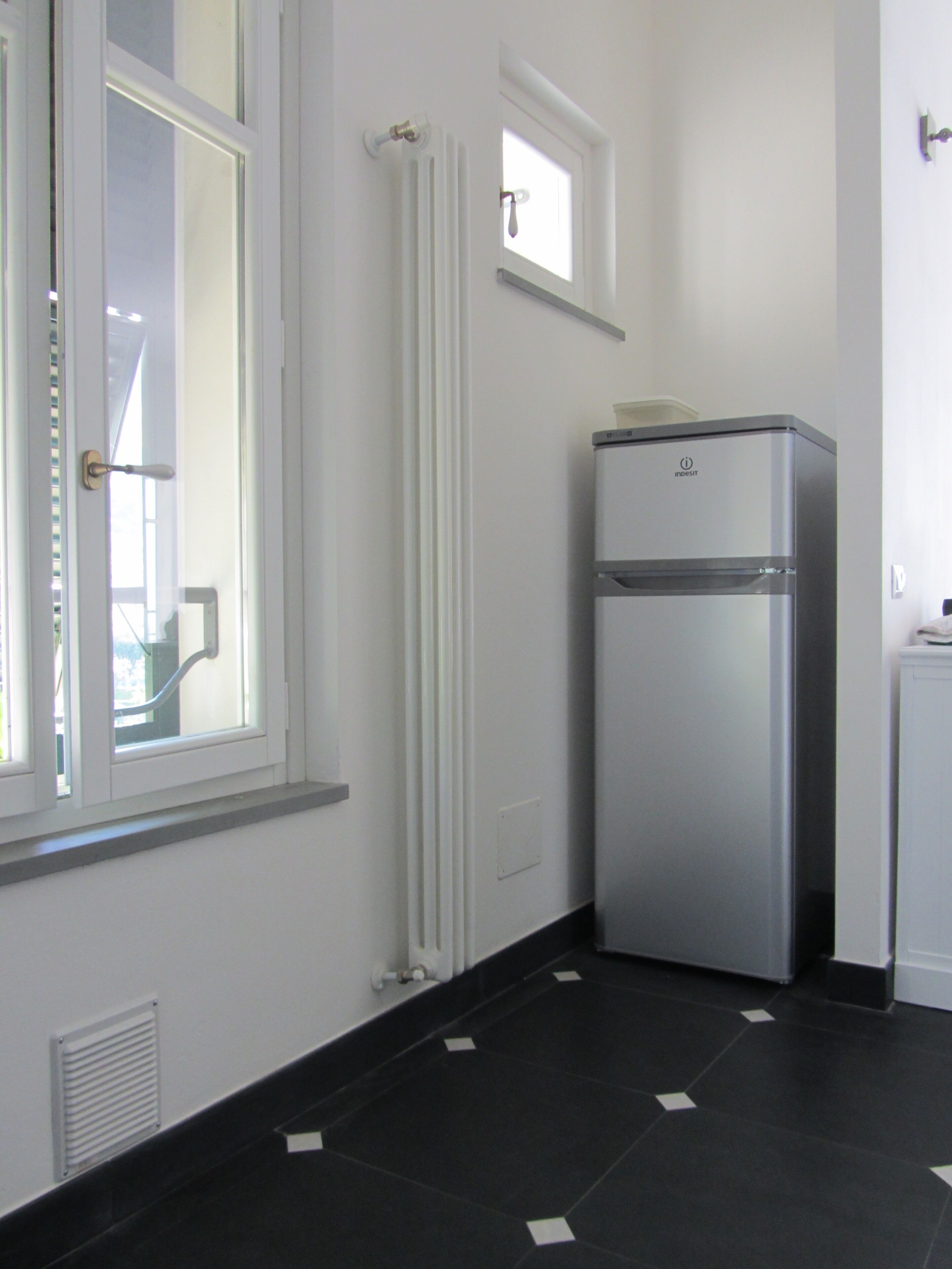 Een keuken met een koelkast, een raam en een radiator.