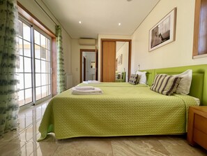 A hotel room with a green bedspread, a large window with curtains, a wooden headboard, and a framed picture on the wall. - Villa Estrelicia, Top Quality, Very Private 3 Bedroom Luxury Villa, Air Conditioning for 6-8 persons (Albufeira,)