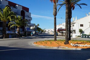 A street with palm trees, a roundabout, and buildings with signs for restaurants and shops. - Villa Estrelicia, Top Quality, Very Private 3 Bedroom Luxury Villa, Air Conditioning for 6-8 persons (Albufeira,)