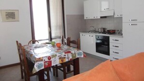 Uma cozinha compacta com armários brancos, um fogão e um espaço de refeições com uma mesa coberta por uma toalha de mesa colorida.