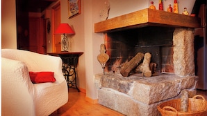 Una sala de estar acogedora con chimenea de piedra, un sillón blanco con cojín rojo, suelo de madera y una cesta de mimbre.