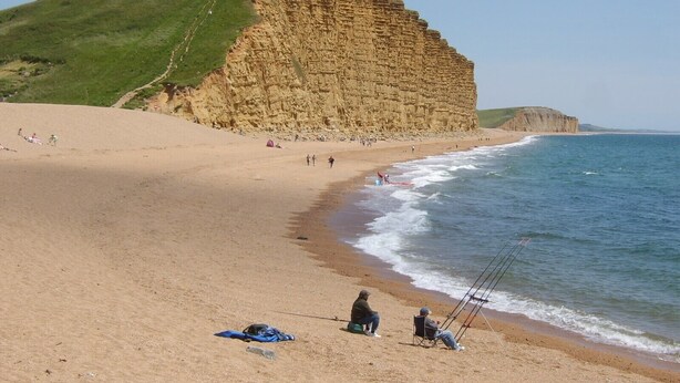 Une plage bordée de falaises, une étendue de sable et des gens qui pêchent.