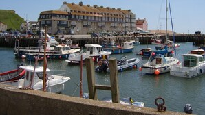Un port de plaisance où sont amarrés différents types de bateaux, un grand bâtiment doté de nombreuses fenêtres et d’un toit en pente, et un ciel bleu dégagé.