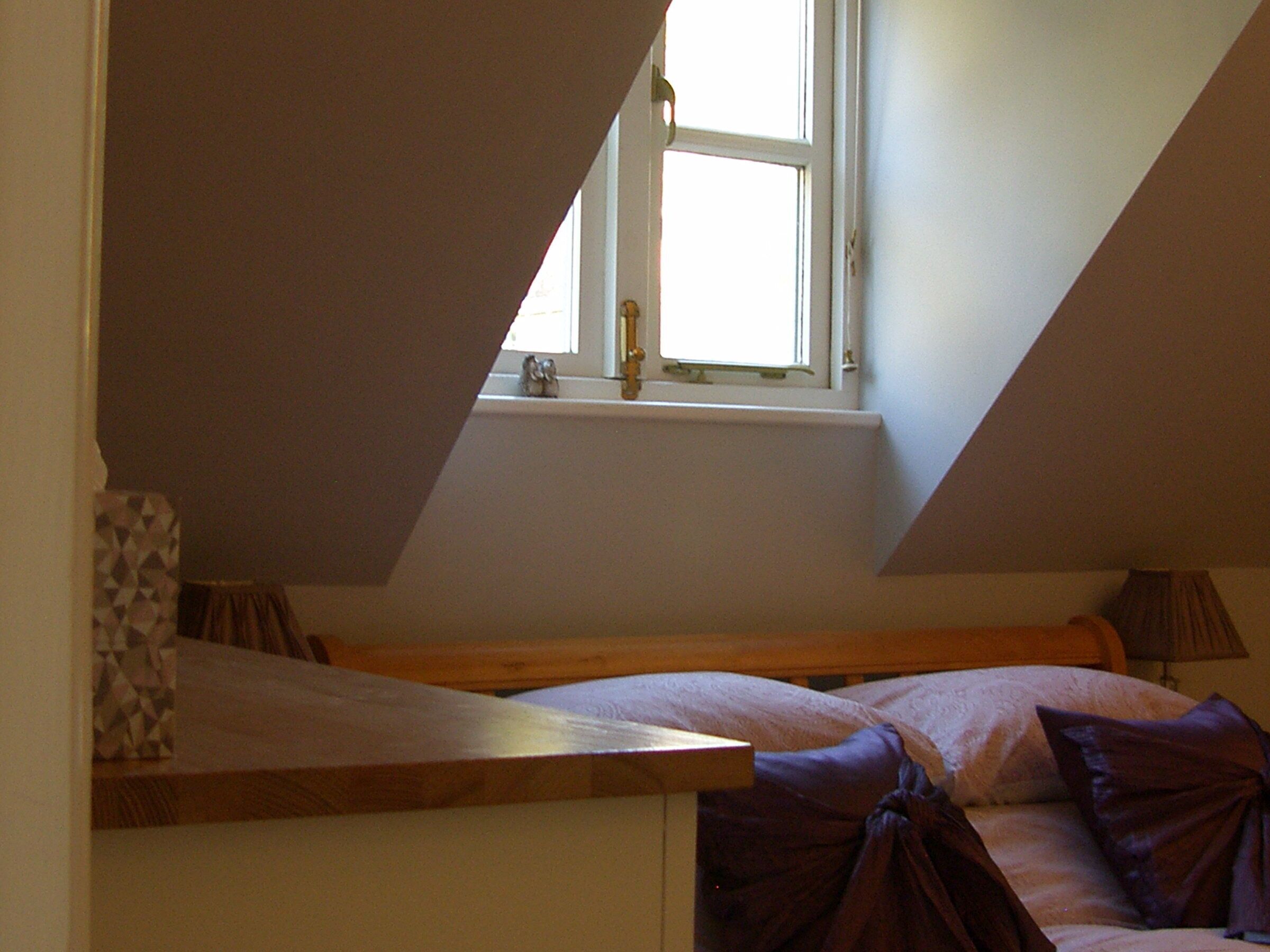 Quarto com teto inclinado, janela e cama com almofadas.