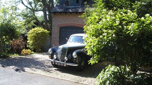 Une voiture ancienne est garée devant une maison à la façade en briques et au toit en pente.