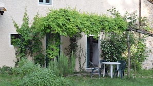 Un bâtiment doté d’un espace jardin comprenant une table et des chaises, entouré de verdure et d’un mur en pierre.
