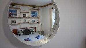 A bedroom with a round mirror, a bed with blue and white bedding, and shelves with framed pictures and small plants. - Luxury V5 | Pool & Jacuzzi | Beach 20 minutes walk | Groups & Families (Albufeira)