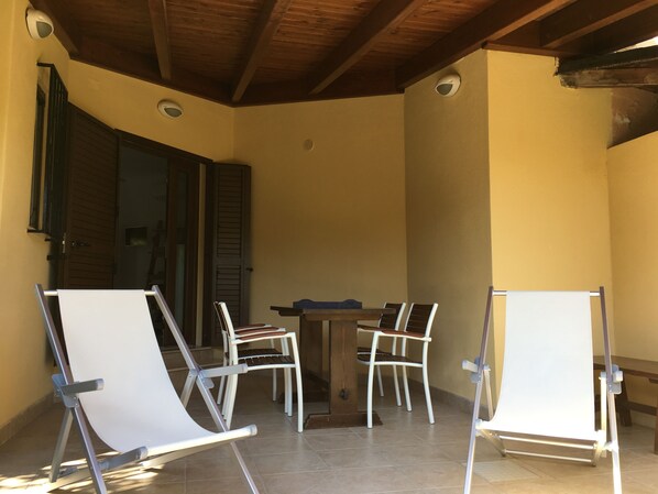 Un patio cubierto con una mesa y cuatro sillas, techo de madera y una puerta con contraventanas.