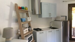 A compact kitchen with a built-in oven, a sink, and a refrigerator. There is a wooden shelf with storage boxes and a lamp on the counter. - Costa Rei chalet 20 meters from the beach (Costa Rei)
