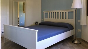A bedroom with a white bed frame, a blue mattress, a bedside lamp, and a small bedside table. - Costa Rei chalet 20 meters from the beach (Costa Rei)