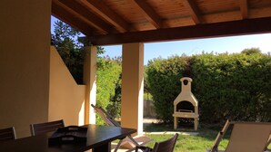 Une terrasse extérieure avec une table et des chaises, un plafond en bois et un four à pizza à l’arrière-plan.