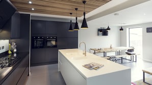 A modern kitchen with a central island, black cabinets, stainless steel appliances, and pendant lighting.