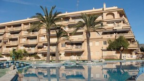 A swimming pool with a reflection of a multi-story building, palm trees, and a clear blue sky. - Modern apartment with great pool, next to harbour, boulevard and beach (el Campello)