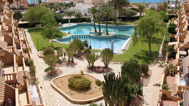 A resort with a central pool, palm trees, and a view of the sea. - Modern apartment with great pool, next to harbour, boulevard and beach (el Campello)