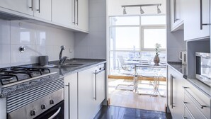A modern kitchen with white cabinets, a gas stove, and a view of the city through large windows. - RENT4REST LISBON PARQUE DAS NAÇÕES 17TH FLOOR RIVER VIEW (Lisboa ciudad)