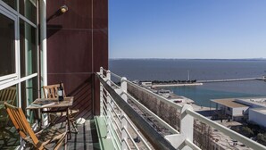 A balcony with a view of the sea, a table with chairs, and a bottle of wine. - RENT4REST LISBON PARQUE DAS NAÇÕES 17TH FLOOR RIVER VIEW (Lisboa ciudad)