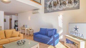 A modern living room with a blue sofa, a yellow sofa, and a glass coffee table. There is a painting of horses on the wall and a sign that reads "ESTRELA". - Estrela da Luz Spectacular Penthouse With Sea And Pool View (Luz)
