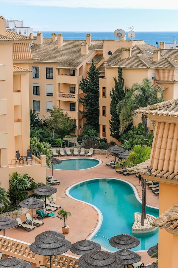 A resort with a central swimming pool, lounge chairs, and umbrellas.