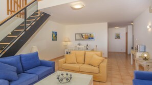 A modern living room with a staircase, a dining area, and a hallway.