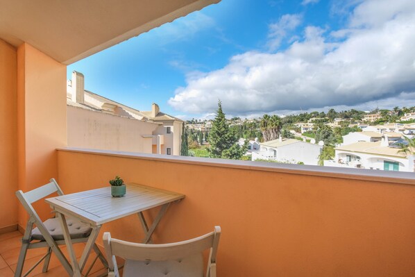 Un balcon avec une table et des chaises, donnant sur un quartier résidentiel avec des maisons et des arbres.