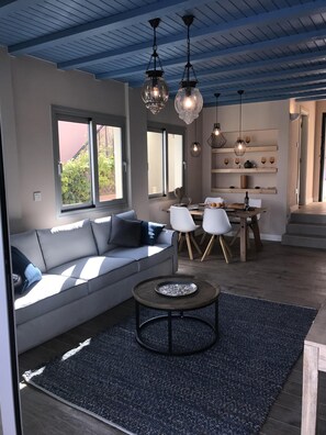 Relax in this stylish living space with a sofa, coffee table, and dining area, offering a view of lush greenery.