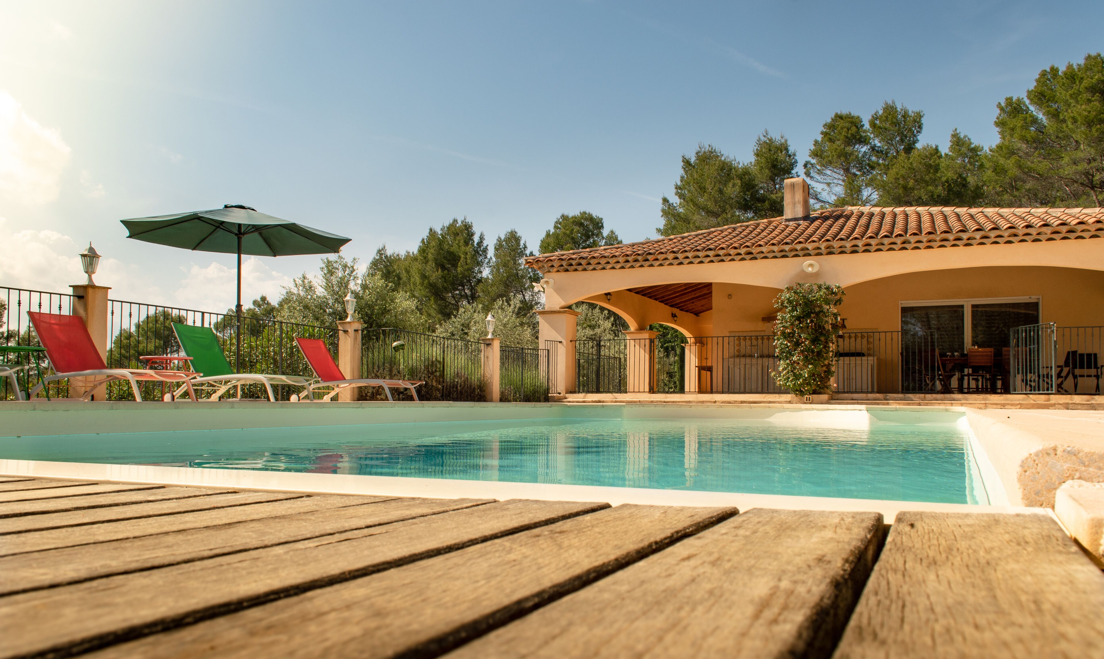 Un espace piscine doté d’une terrasse en bois, de chaises longues et d’un patio couvert.
