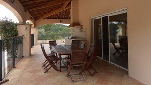 A covered patio with a wooden table and chairs, a sliding glass door, and a view of a forested hill. - House / Villa - DRAGUIGNAN (Draguignan)