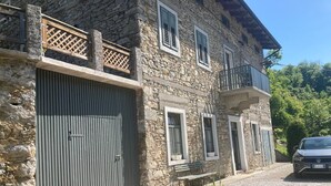 A stone building with a large garage door, a balcony with a lattice railing, and a parked car. - Farmhouse in Klavze, Most na Soci, Primorska, Slovenia - Peaceful Location (Klavže)