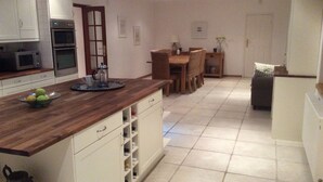 A modern kitchen with white cabinetry, a wooden countertop, and a dining area with a table and chairs. - Farmhouse in Klavze, Most na Soci, Primorska, Slovenia - Peaceful Location (Klavže)