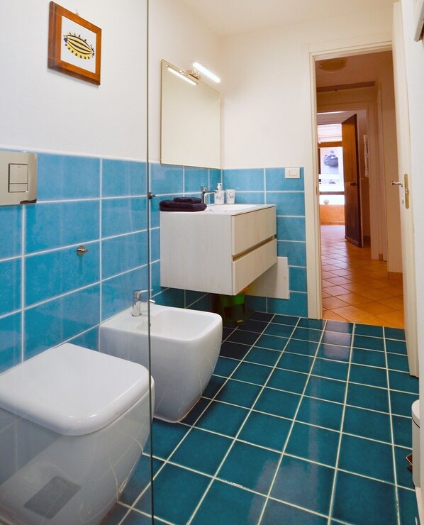 A bathroom with blue tiled walls, a white sink, and a toilet. - Calaverde, very refined apartment a stone's throw from the sea (Pula)