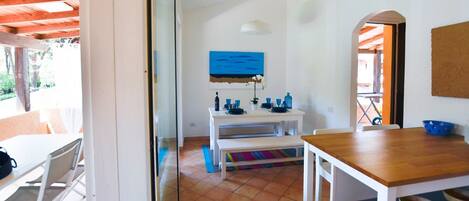 A bright room with a white table, a wooden table, and a bench. There is a blue painting on the wall.