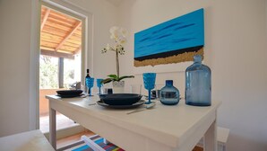 A dining area with a white table, blue glassware, a white orchid, and a blue painting on the wall. - Calaverde, very refined apartment a stone's throw from the sea (Pula)