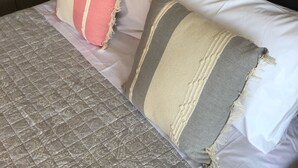 Un letto con copripiumino grigio a motivi, due cuscini sfilacciati e una testiera nera.